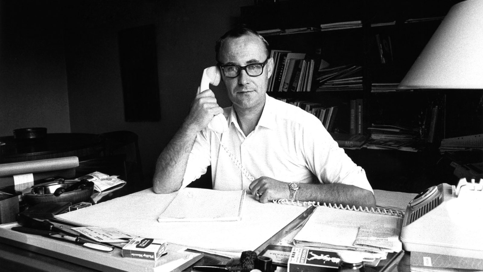 Ein Schwarz-Weiß-Foto von Ingvar Kamprad, der an seinem Schreibtisch sitzt und sich Notizen macht, während er telefoniert.