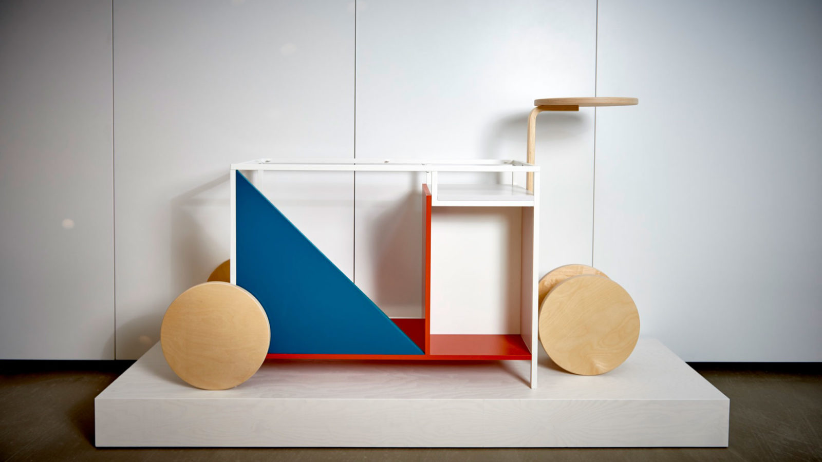 En konceptmöbel gjord av vita, röda, blå och omålade geometriska former i trä.