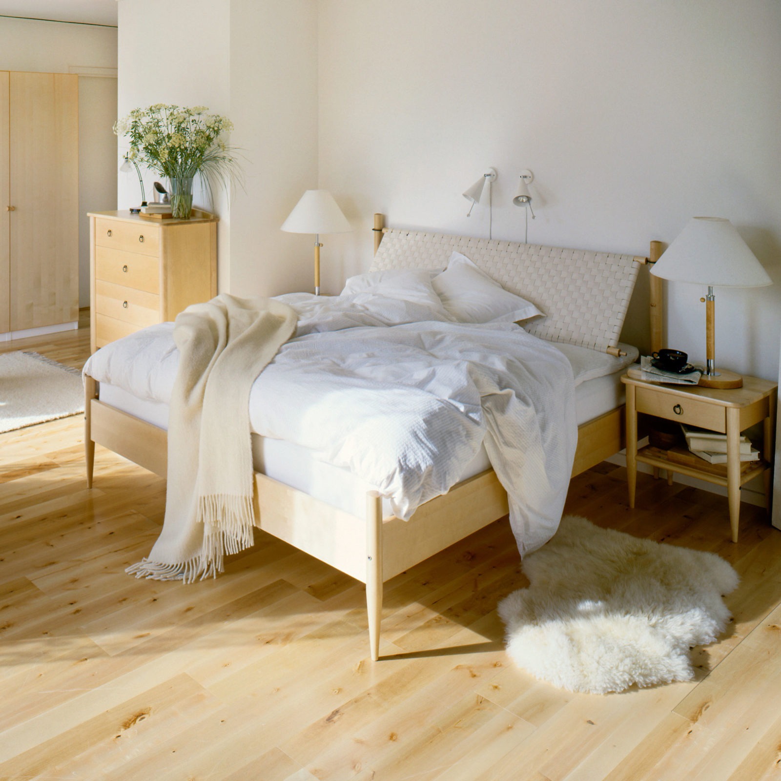 Scandinavian style bedroom with white bedlinen and furniture in light birch and soft, simple shapes.
