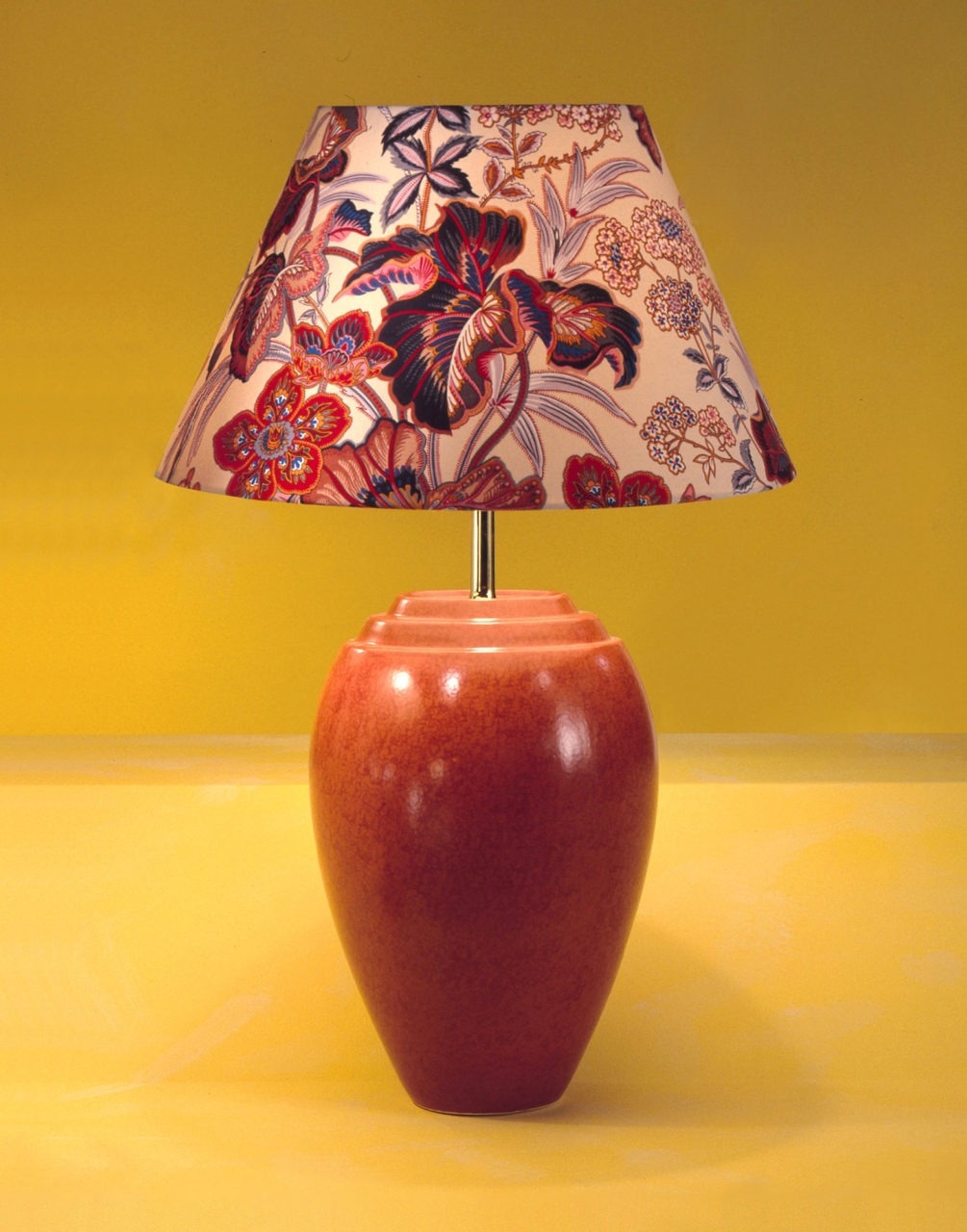 Bordslampa med fot i brun keramik och lampskärm i blommönster i blått och rött.