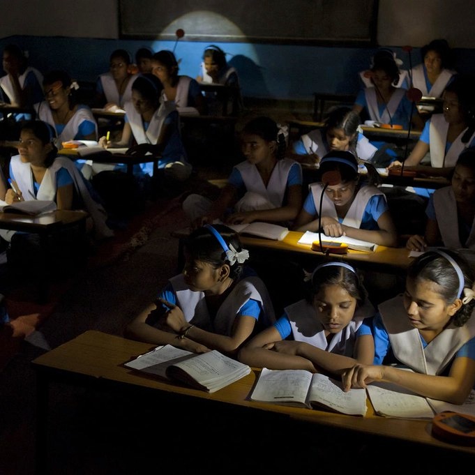 Dark classroom filled with girls who are studying with help of small yellow lamps on their desks.