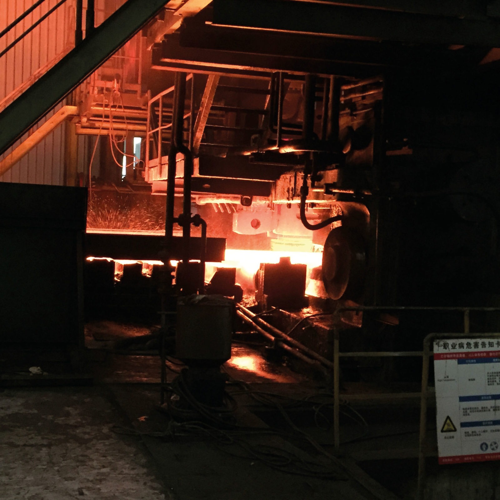Stor fabriksmaskin lyser upp mörker med orange och röda svetsgnistor och upphettad metall.