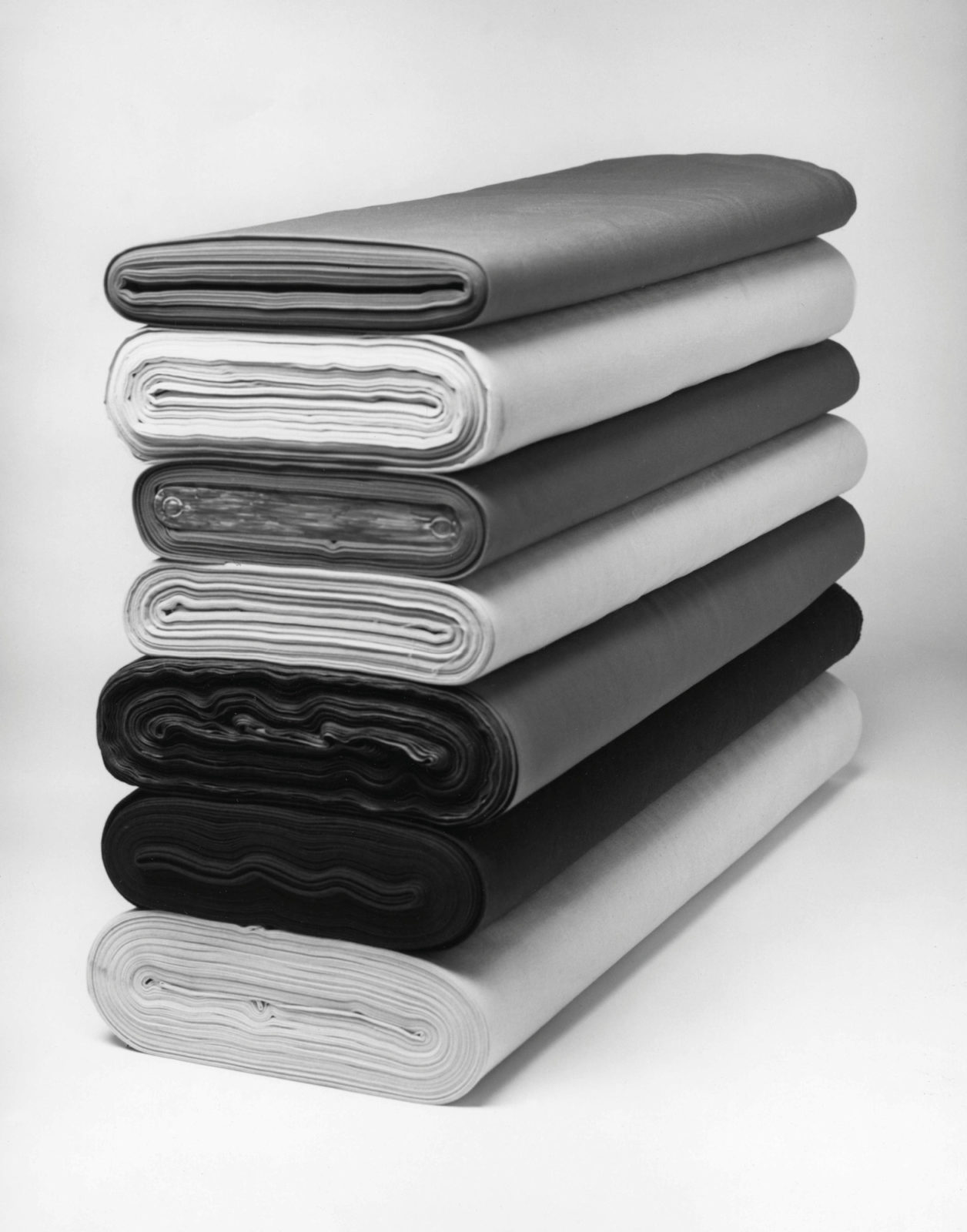 Fem rullar textil i svart och grått, staplade på varandra.