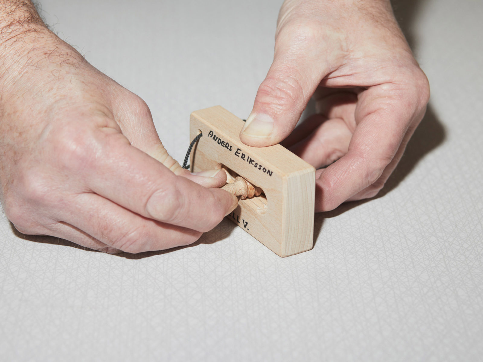 Händer håller ett litet träblock med ett hål i, och en liten träplugg. Anders Eriksson står skrivet på blocket.