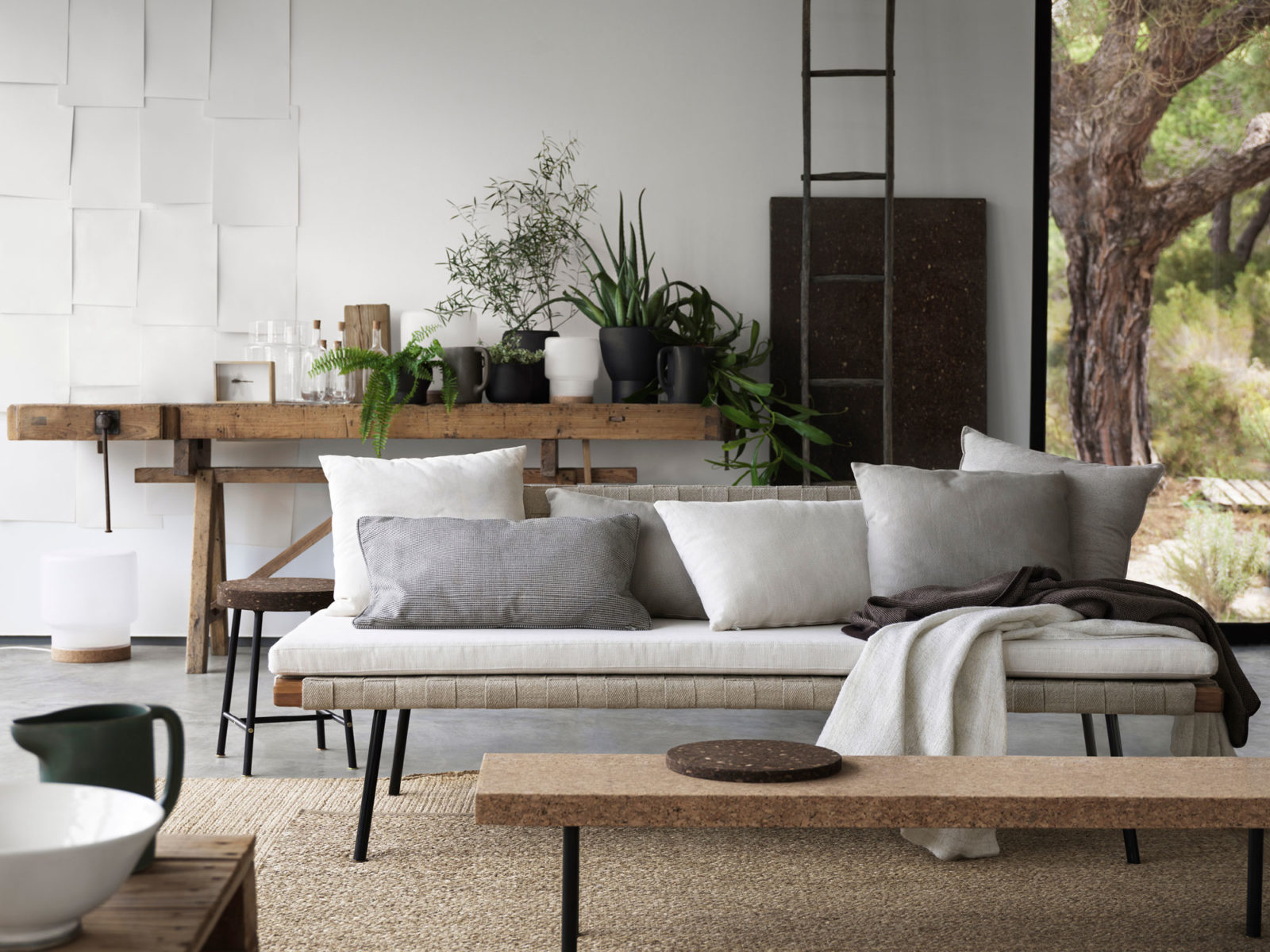 Interiör med gröna växter, soffa, pallar, bord, bänk i naturmaterial som kork, trä och bambu.
