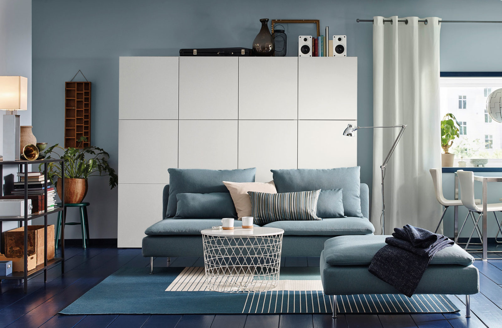 Vardagsrum i modern stil i blå och vita toner med mörkblått trägolv, blå soffa, vita bord och skåp.