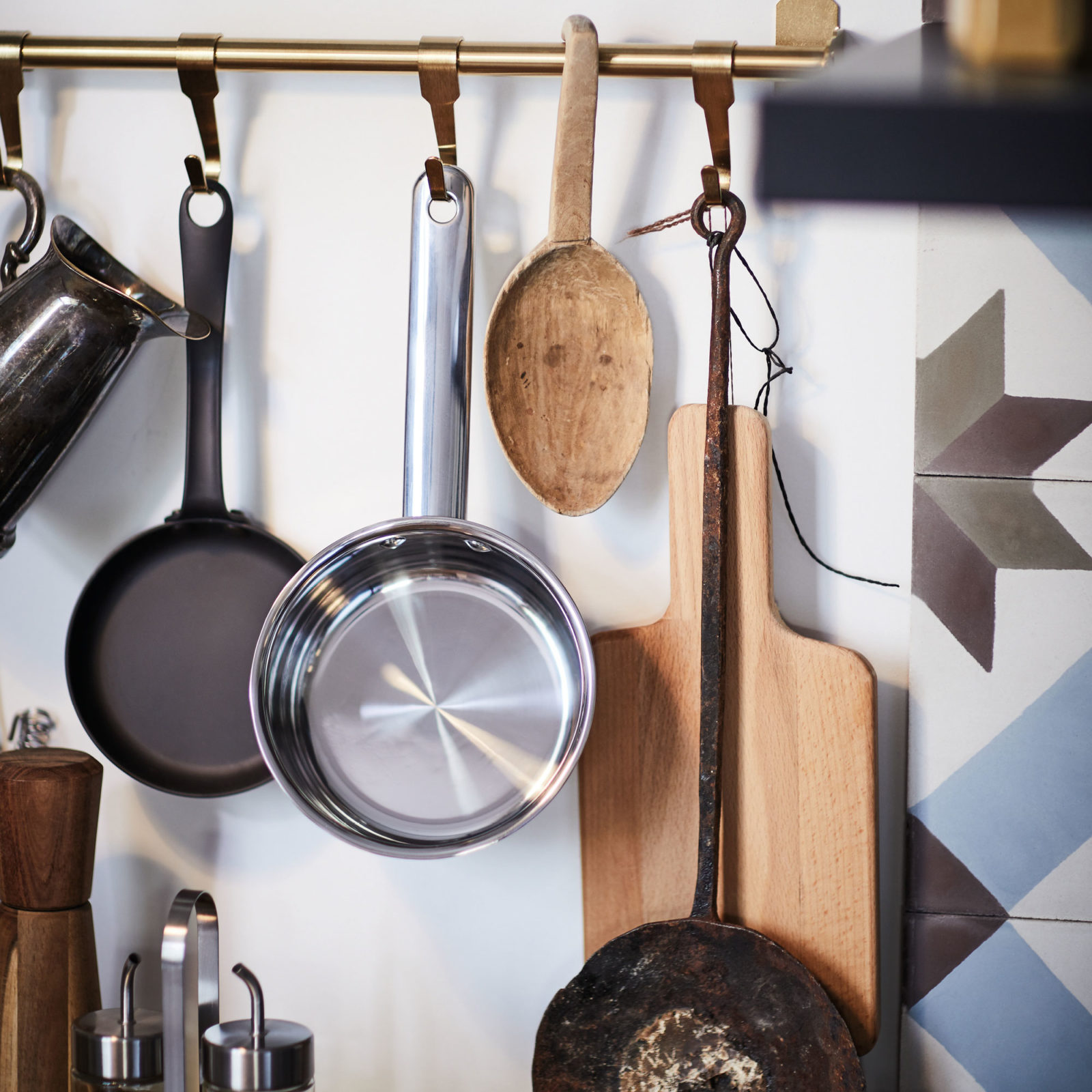 Close up of kitchen utensils, cutting board and pots hanging on hooks on the wall.
