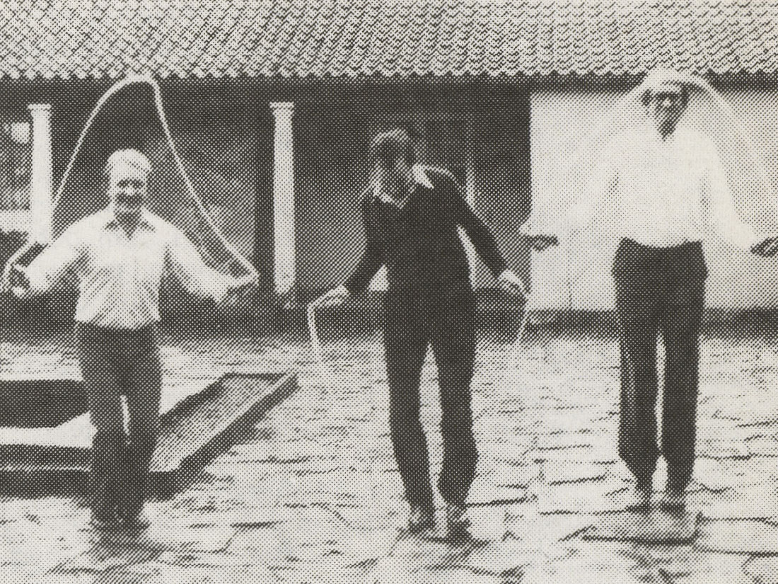 Newspaper picture of three laughing men skipping rope together outdoors.