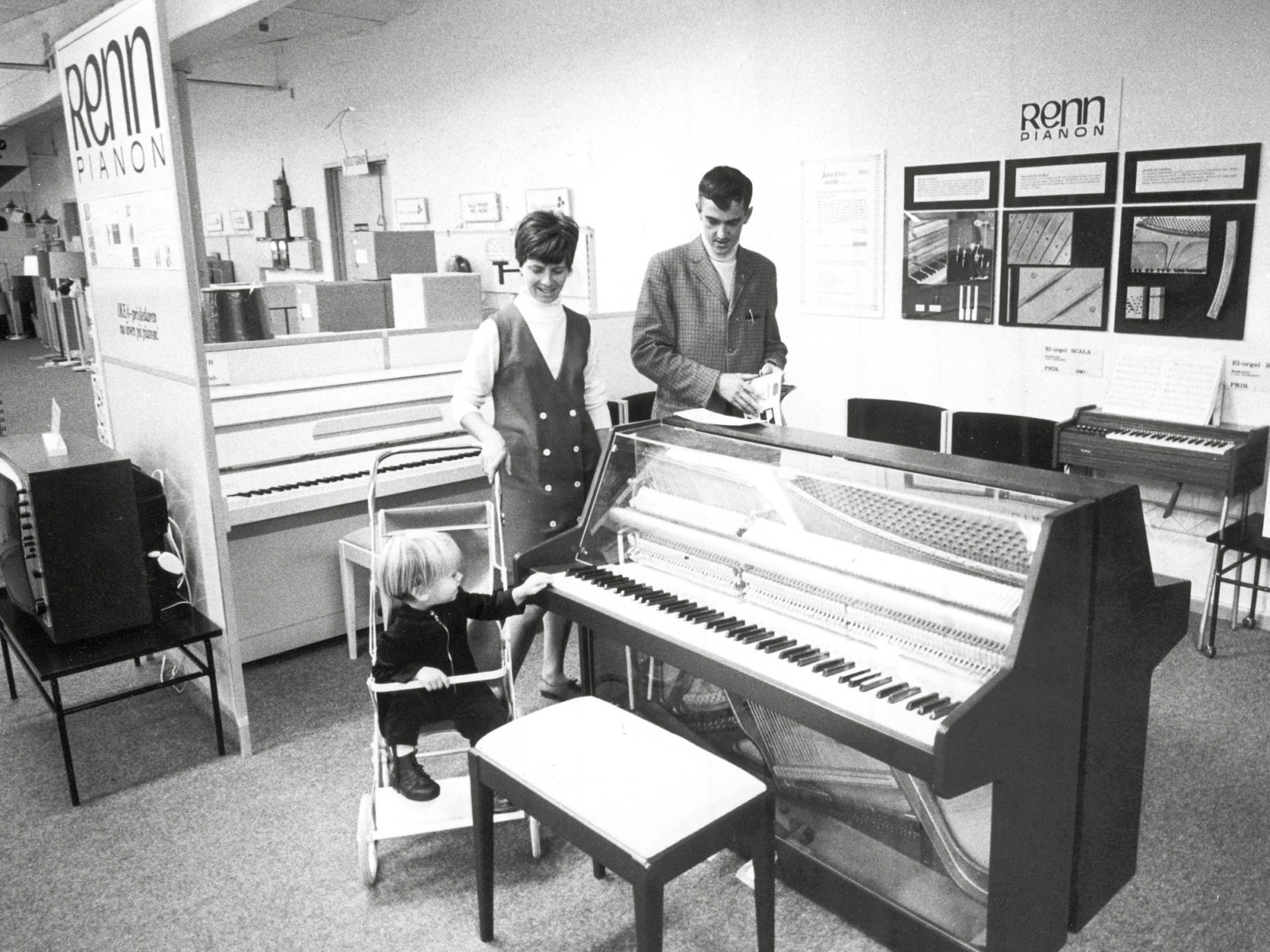 Jeune famille, homme, femme et enfant en poussette, regarde des pianos exposés dans un showroom IKEA en 1973.