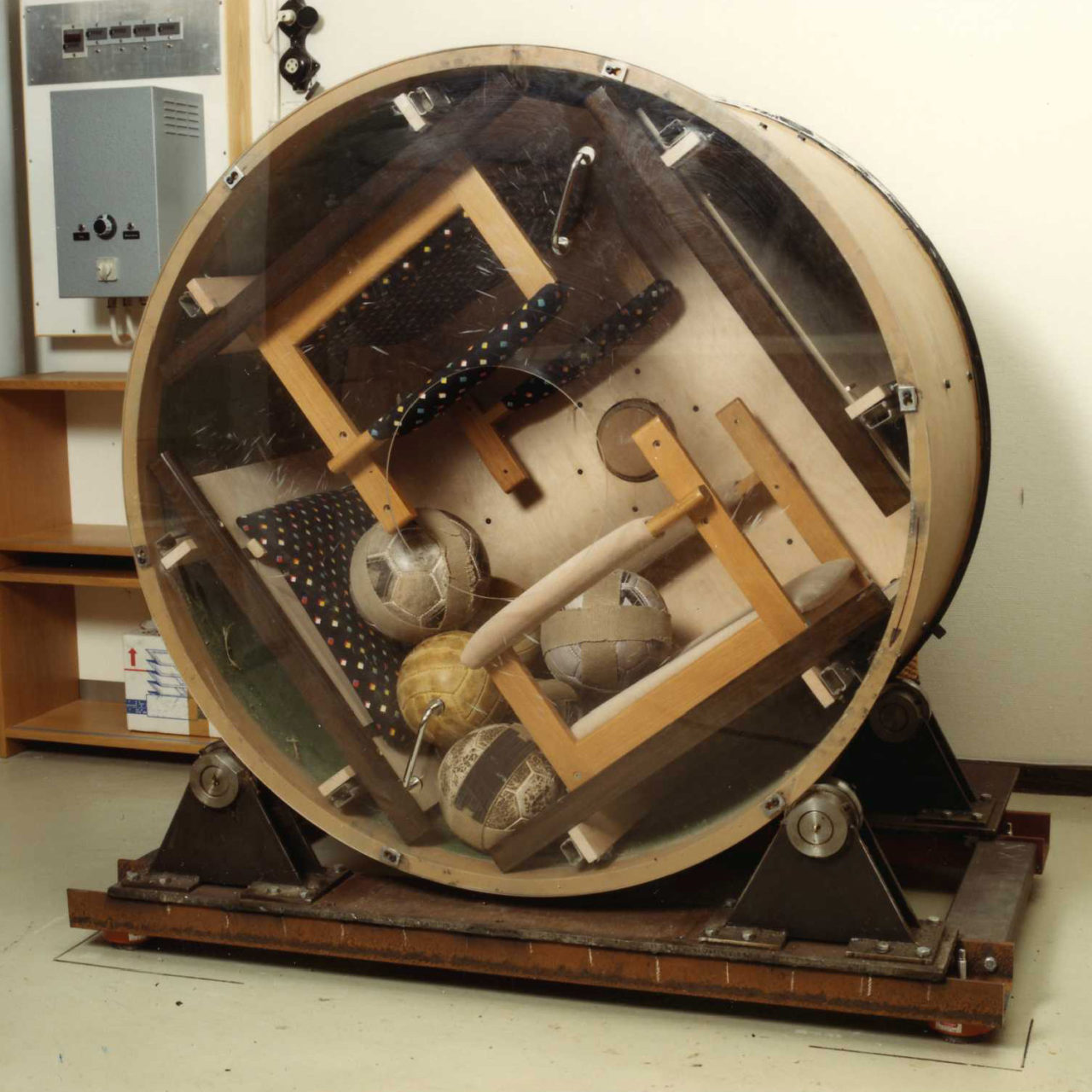 Crudely built testing machine, a spinning round shape in which armchairs are being pounded by soccer balls.