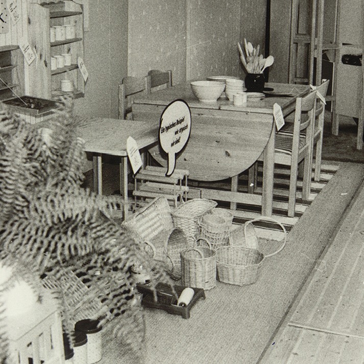 1970s photo from IKEA store with a mixed display of woven baskets, pine tables and chairs.