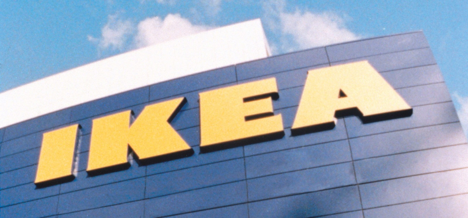 Blue ikea store facade against light blue sky. Giant yellow letters on the facade form the word IKEA.