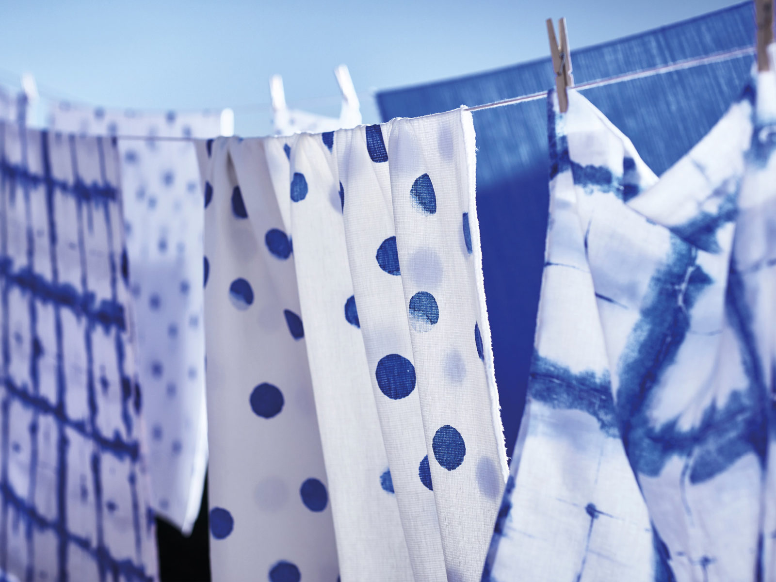 Textiles in different blue and white patterns hanging on clothes line against blue sky.