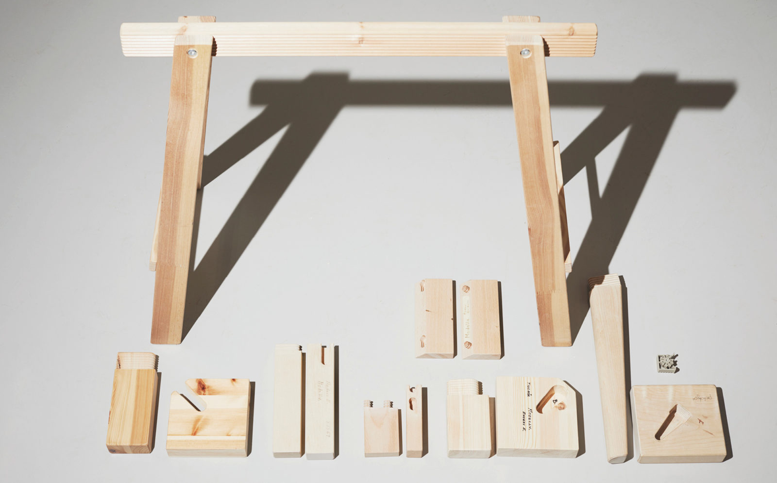 A wooden trestle and several differently shaped parts, wooden prototypes, laid out on the floor.