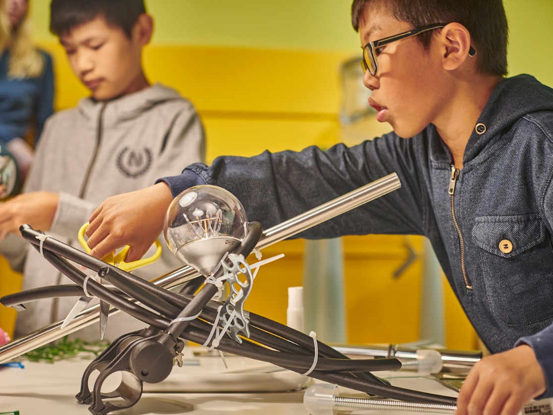 Zwei Jungen bauen neue Dinge aus alten IKEA Produkten wie einer Schiene, einer Glühbirne und einem Kunststoffrohr während eines Workshops im IKEA Museum.
