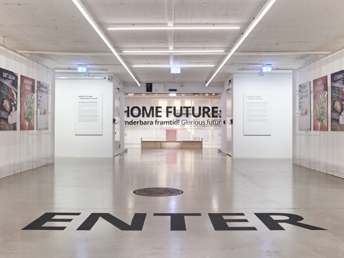 White walls, photo posters and “ENTER” in large writing on the beige stone floor of the entrance to IKEA Museum.