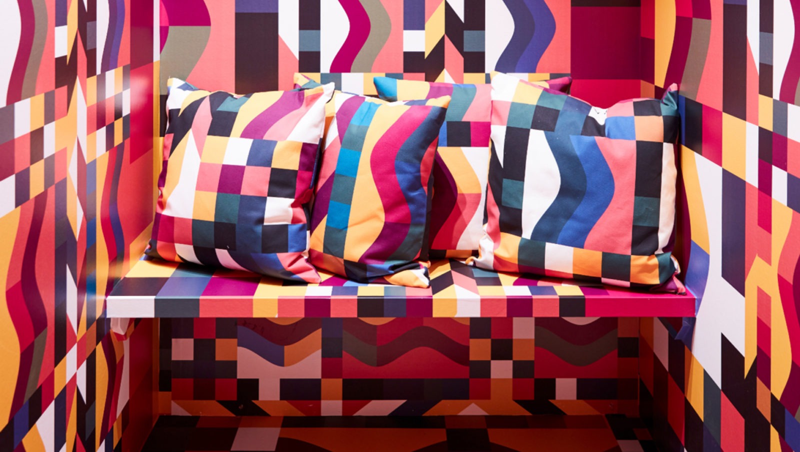 A tiny space with just one bench with pillows. They, and all the surfaces, are covered with a bold, colourful, graphic pattern.