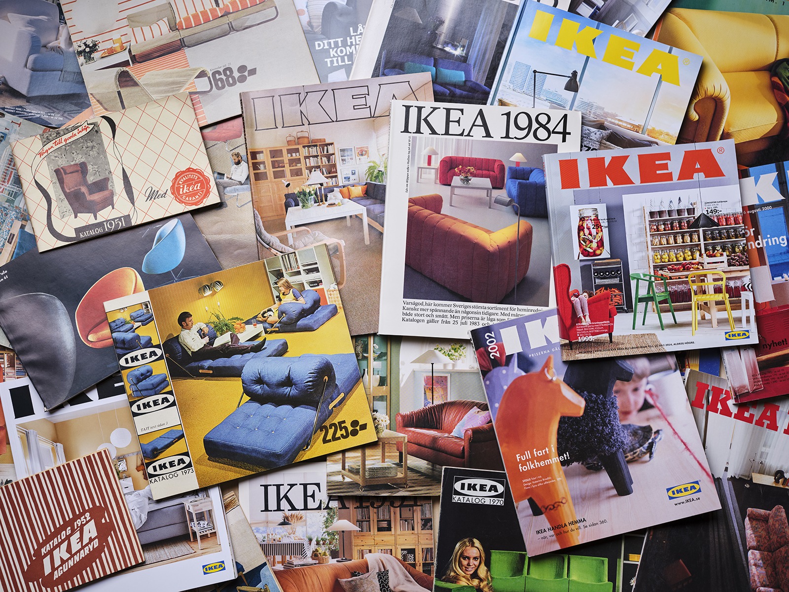Mehrere Ausgaben des IKEA Katalogs von 1951 bis heute, die sich überlappen und eine große Fläche bedecken.