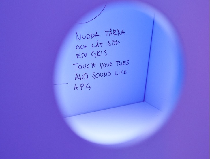 Der handgeschriebene Text „Touch your toes and sound like a pig“ ist durch ein violettes Guckloch zu sehen.