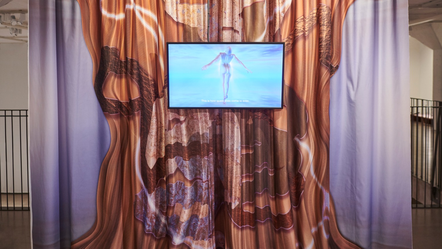 Ein hellvioletter Vorhang mit einem aufgemalten, braunen Muster und ein Bildschirm mit einer nackten, in grünblauen Leuchtfarben getauchten Person.