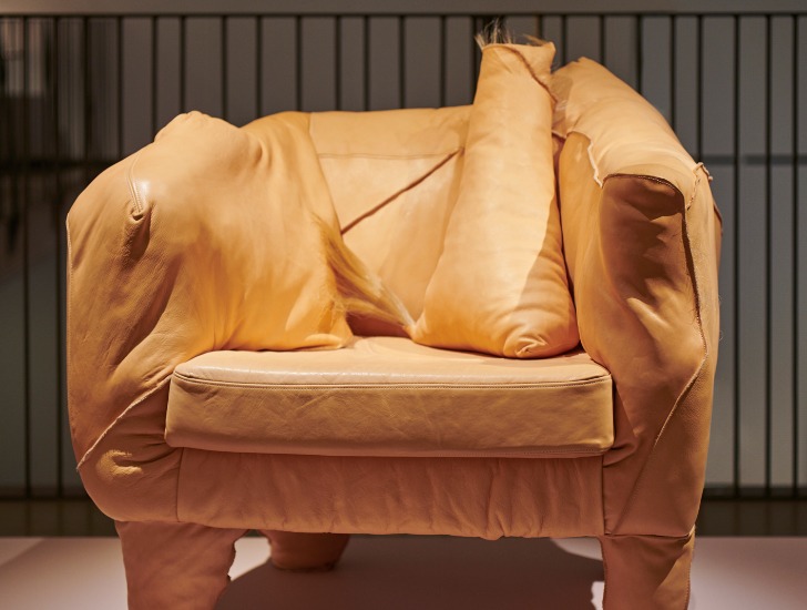 Ein asymmetrischer Sessel mit einem unordentliche Falten werfenden, hellbraunen Lederbezug namens „Uncanny Traces“.