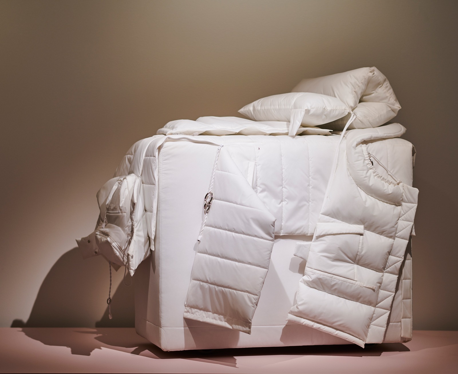 En vit resväskeformad konstruktion täckt med delar av en vit dunjacka och en liten kudde.