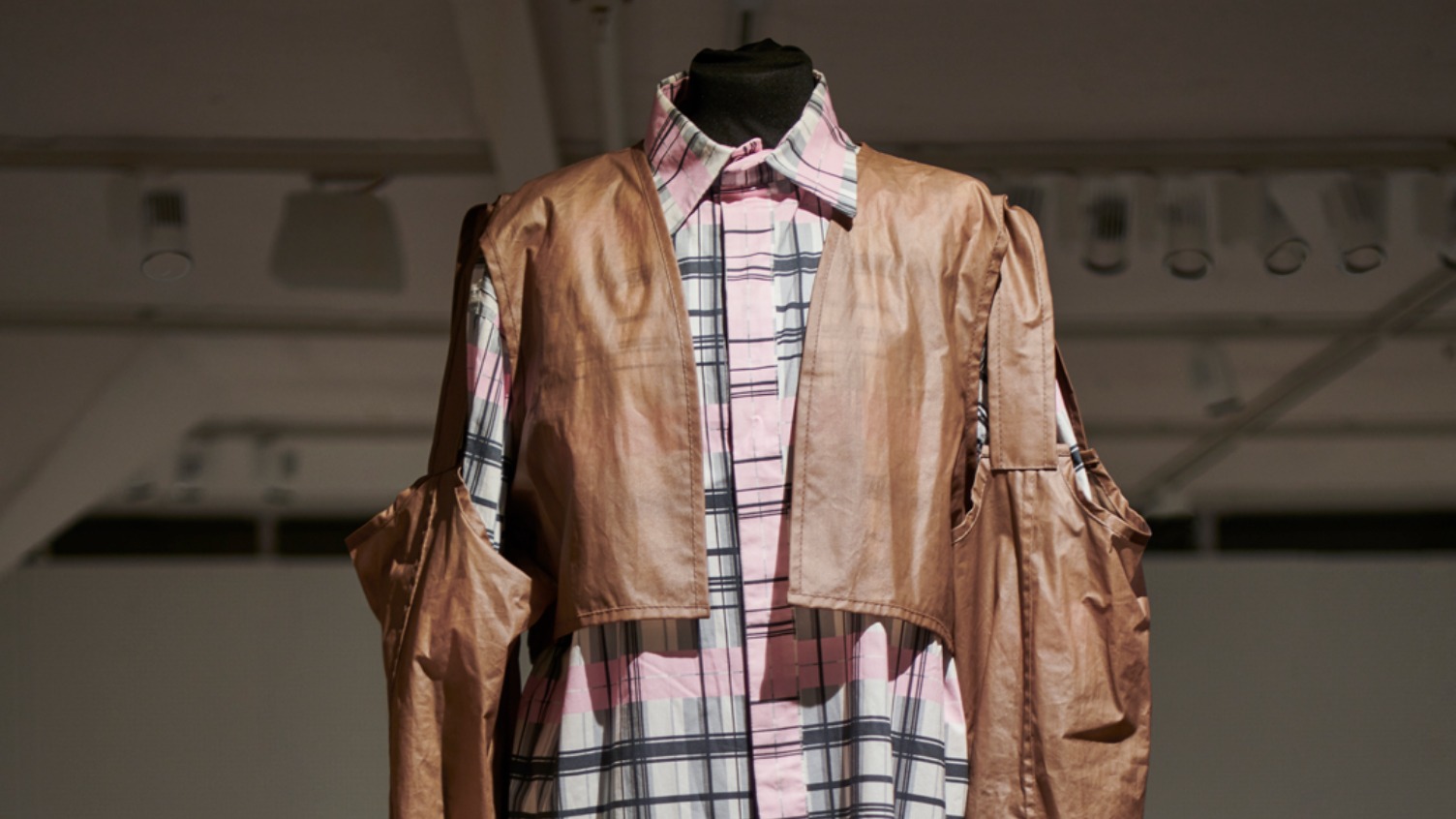 En rutig långskjorta och byxor i rosa och grått och en halvgenomskinlig, brun dekonstruerad jacka med många fickor.