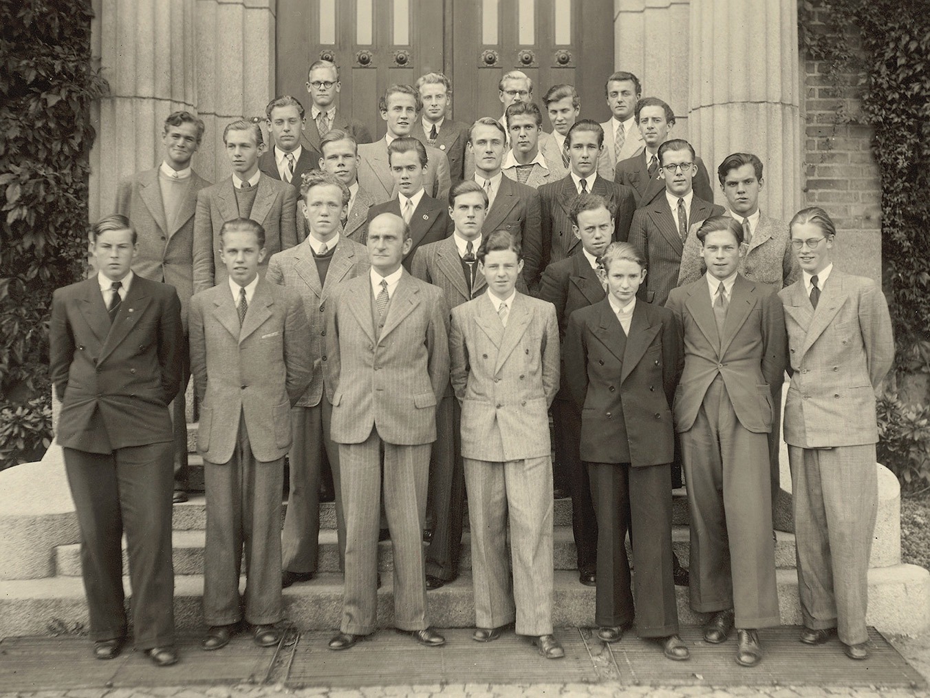 Gruppfoto, unga män i ljusa 1940-talskostymer uppställda i fem rader framför imponerande byggnad. Ingvar Kamprad i mitten.