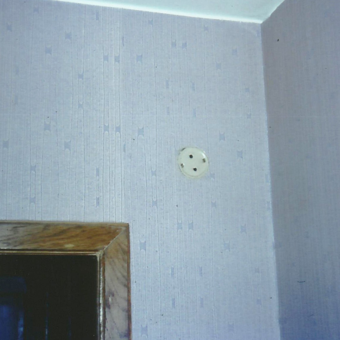 Gros plan sur une bouche d’aération sur un mur, tapisserie bleu clair au mur.