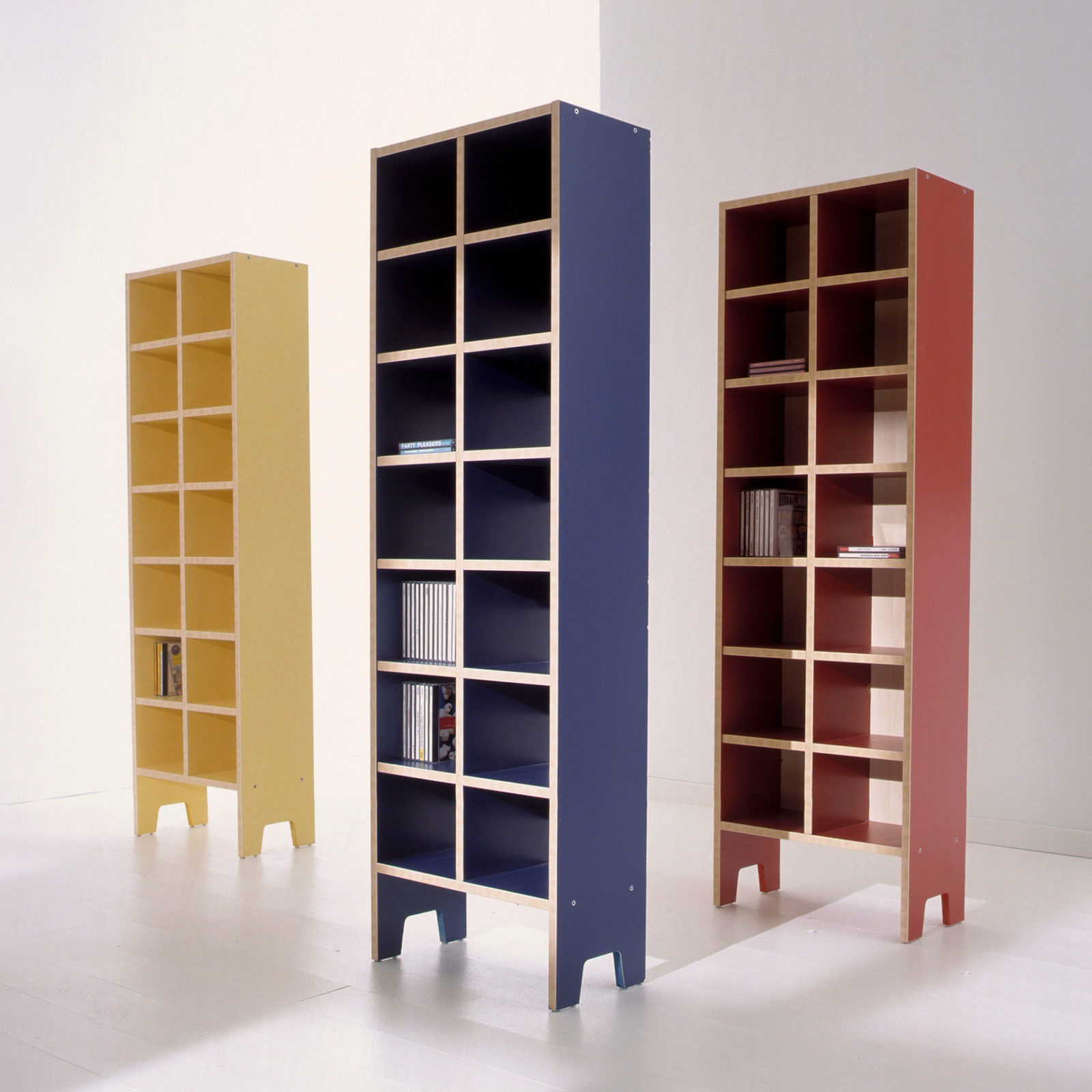 Three high free-standing ROBIN shelves made of dyed particleboard – in yellow, red and blue, with birch-coloured edging.