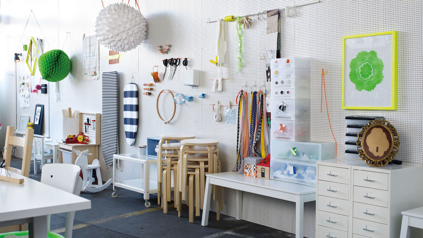 White wall holds tools, textiles, ironing boards and decorations. In front are stacked stools, tables and storage.