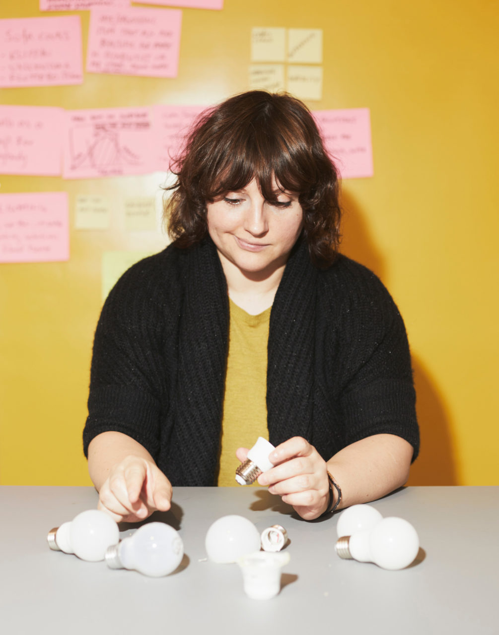 Paulina Pajak, sentada en una mesa donde hay piezas de una bombilla led, sostiene una pieza y señala otra con cara pensativa.