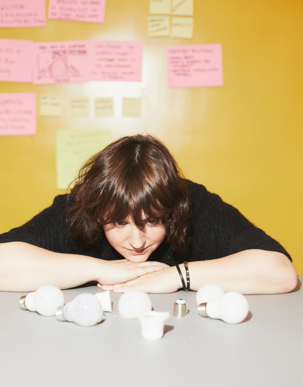 Paulina Pajak, resting chin on hands, looks at LED bulb parts scattered on grey table top.