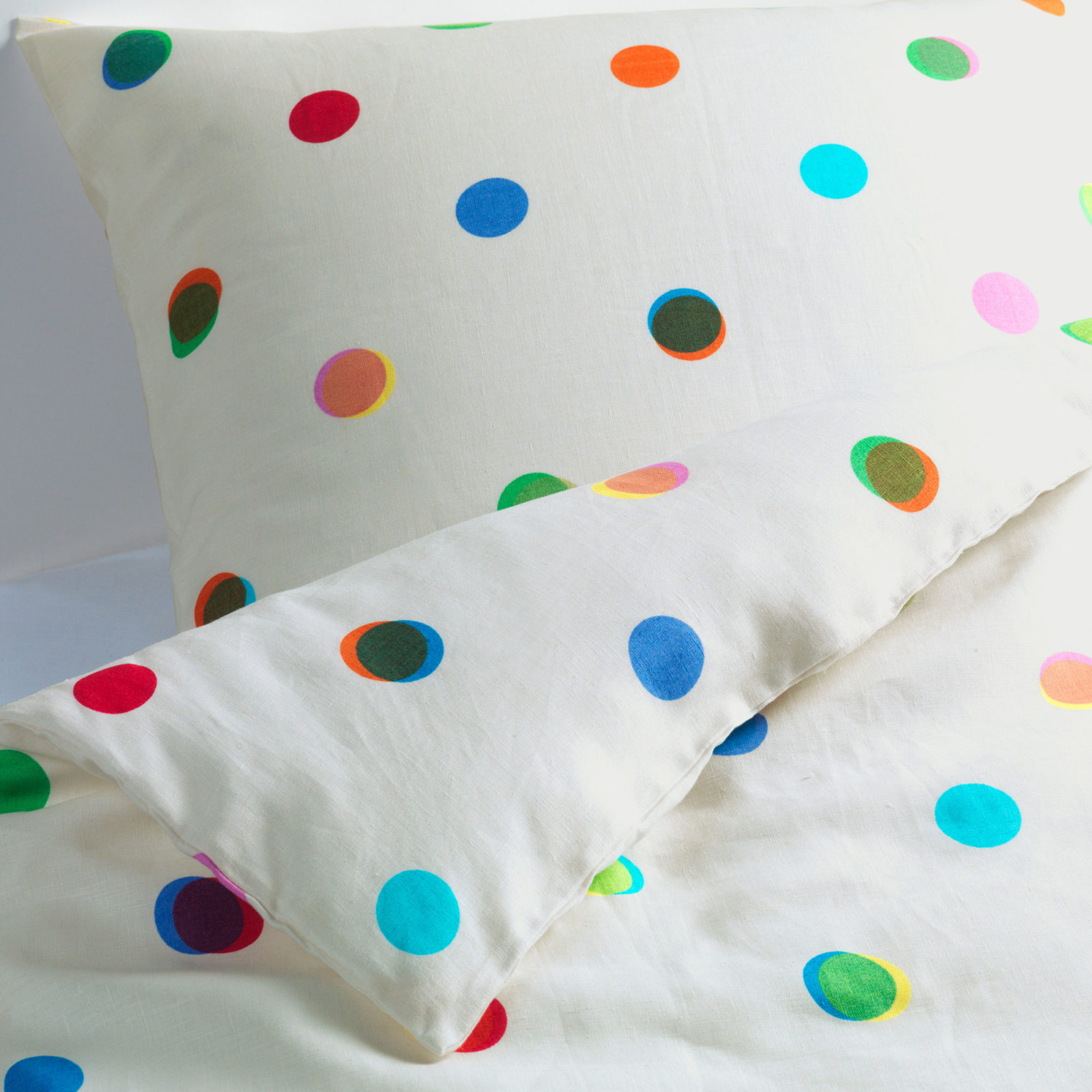 White quilt cover and pillow case with different coloured dots overlapping each other.