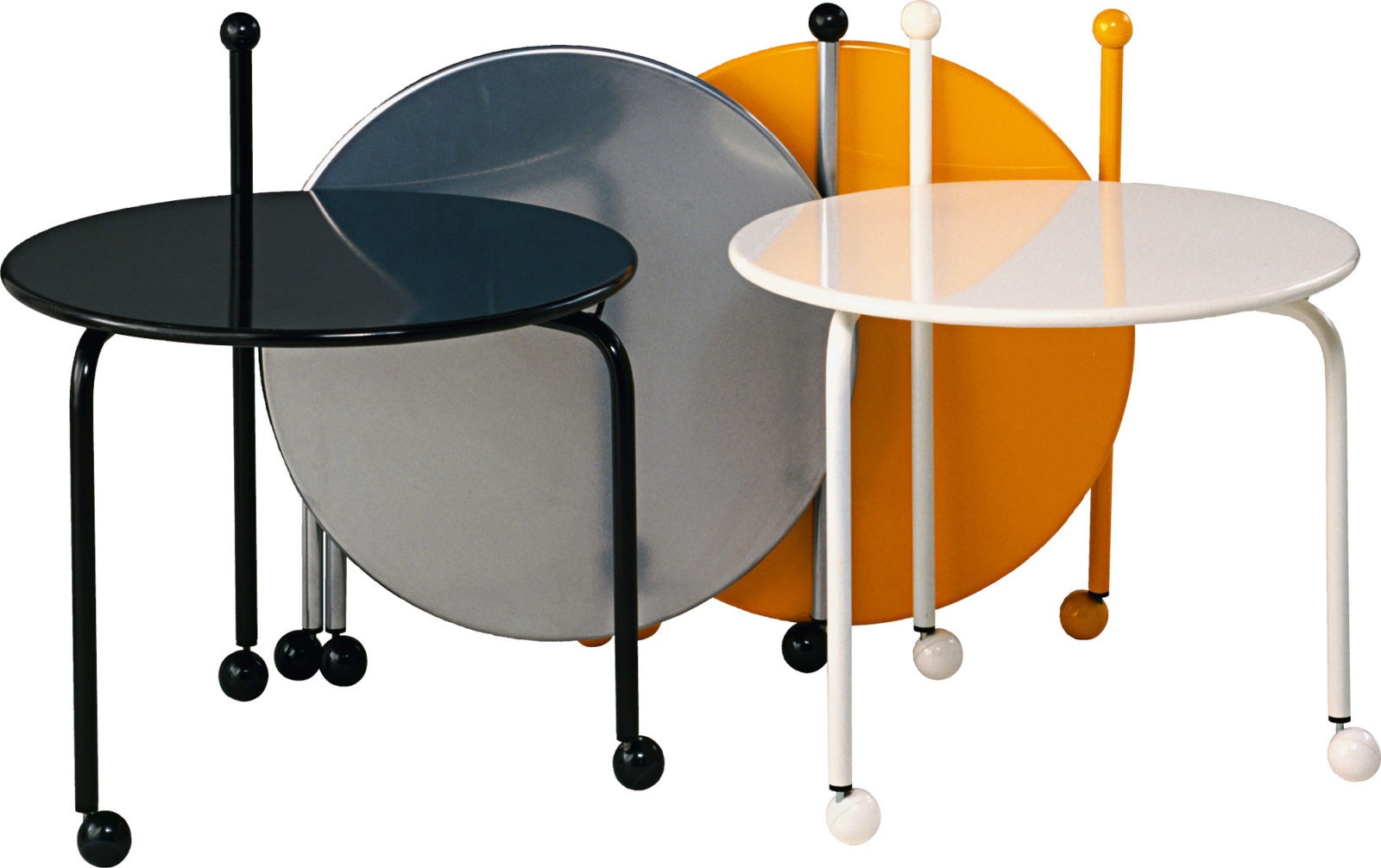 Four round foldable coffee tables on castors, in different colours, two of the table tops are folded up.