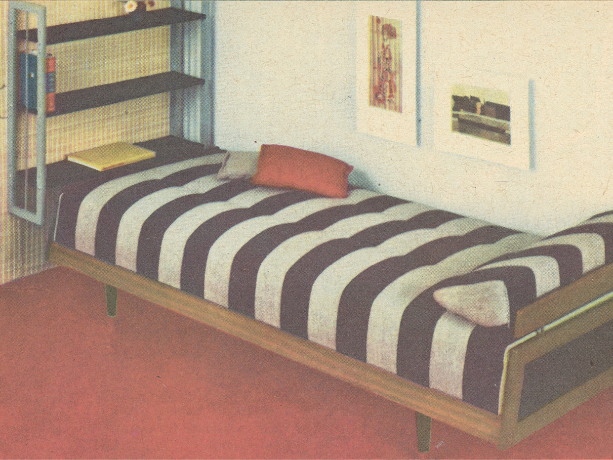 Bett mit braun-weiß gestreifter Tagesdecke. Gestell aus braunem Holz. Am Fußende ein an der Wand montiertes Regal.
