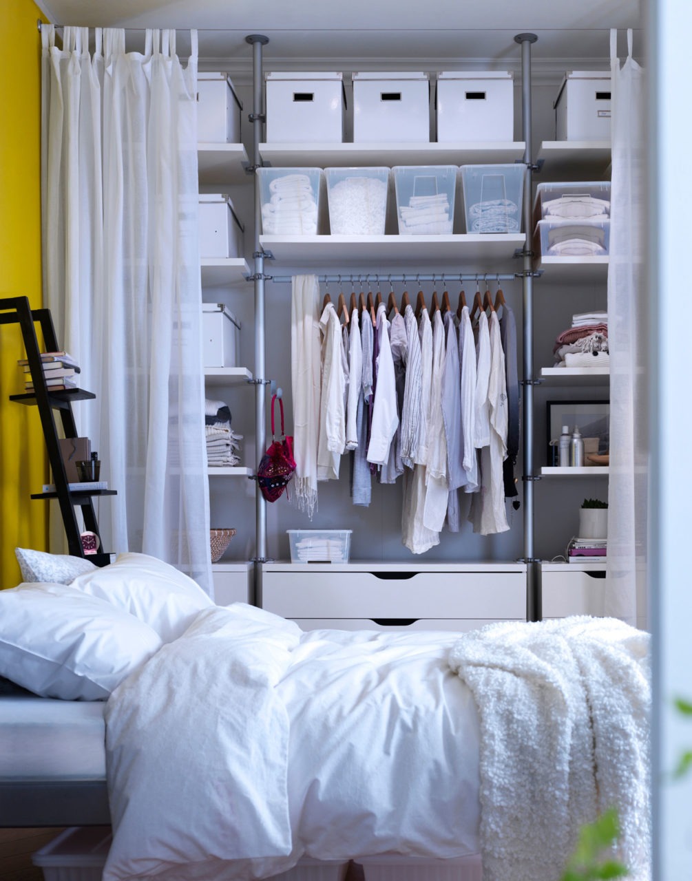 A light bedroom where one wall is covered by a storage combination with open and closed storage. A drape can be pulled across.