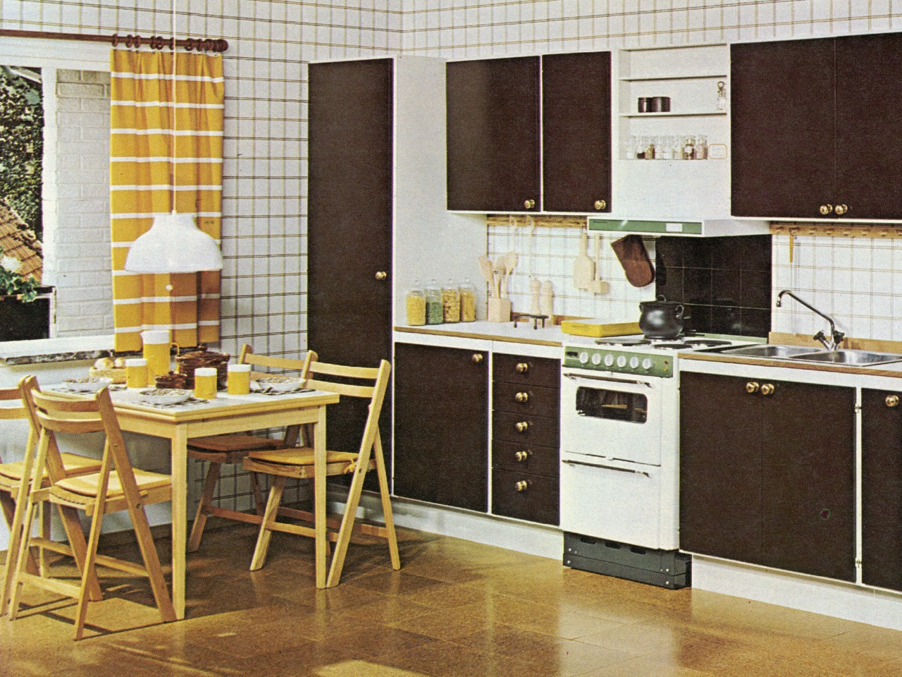 A kitchen with cork pattern flooring, brown cabinet doors, white cooker and dishwasher, checked white wallpaper, and wooden dining table and chairs.