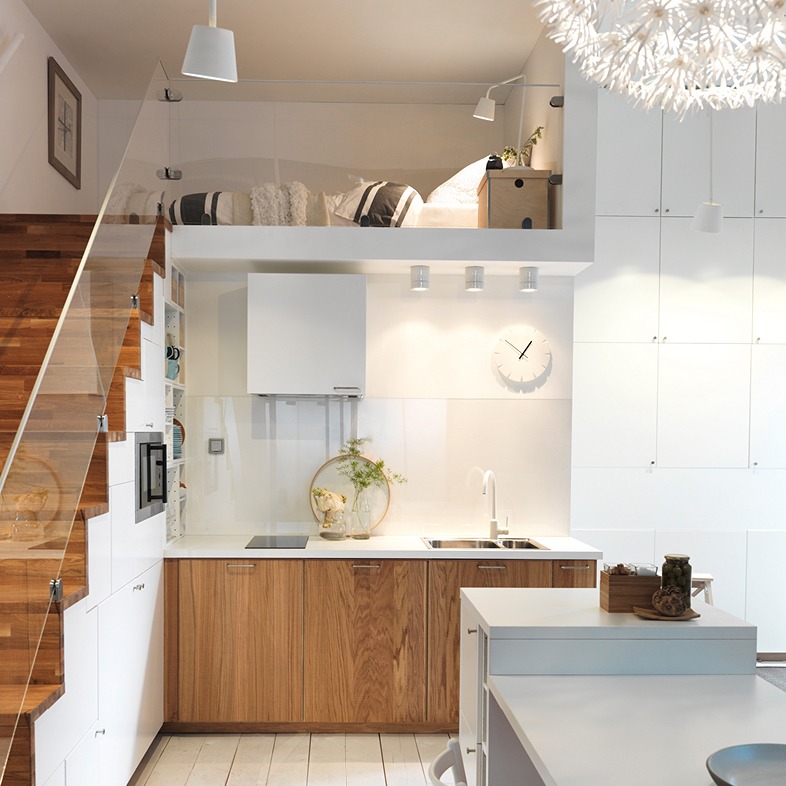 A kitchen next to a staircase that goes up to a sleeping loft. The kitchen cabinets and steps are clad in veined wood, everything else is white.
