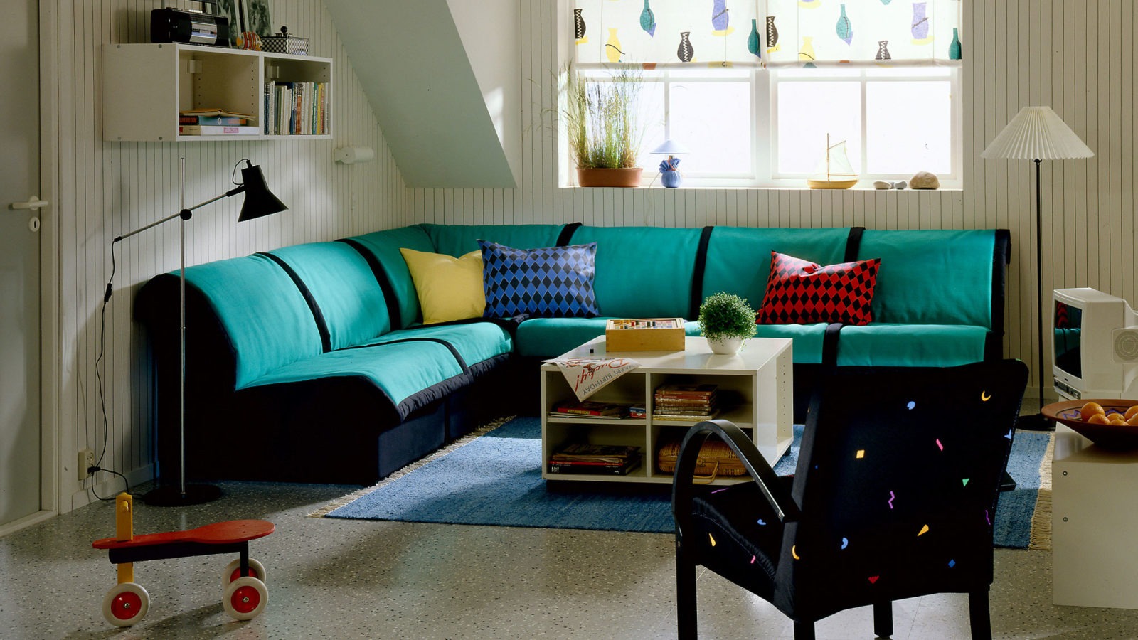 A light room with a black and green modular sofa, model LEXBY, arranged as a corner sofa. Colourful patterned textiles.