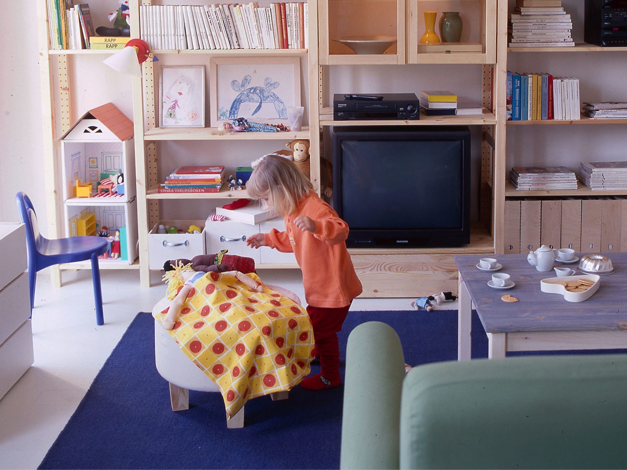 A living room where a well-filled IVAR storage combination in light wood covers the wall. A young child is playing nearby.