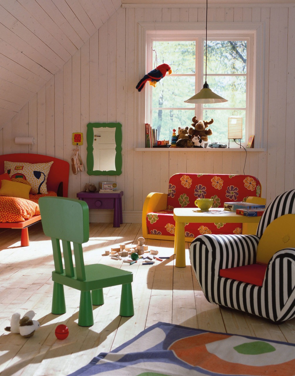 Färgglada möbler i bullig stil, modell MAMMUT, samt spridda leksaker i ett rum med golv, väggar och snedtak i ljust trä.