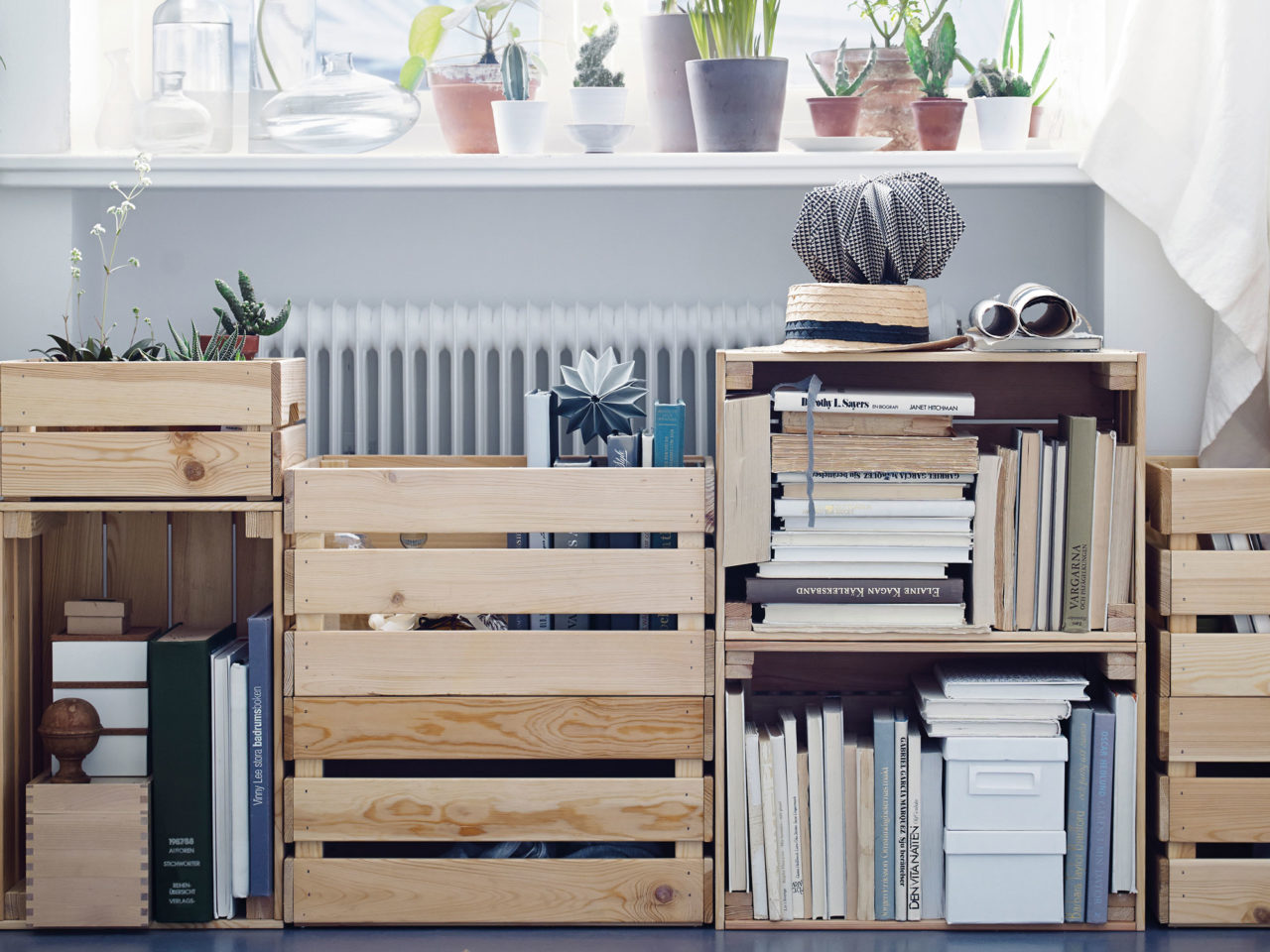 Libros y objetos llenan un mueble compuesto íntegramente por cajas de madera, modelo KNAGGLIG, apiladas en distintos niveles.