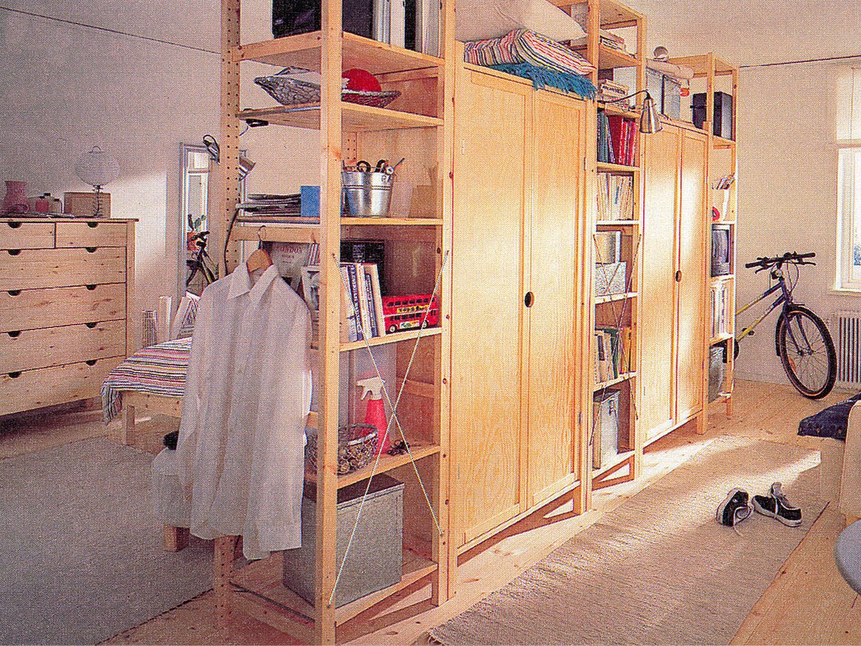 Raum mit großer, prall gefüllter IVAR Aufbewahrungskombination aus hellem Holz als Raumteiler.