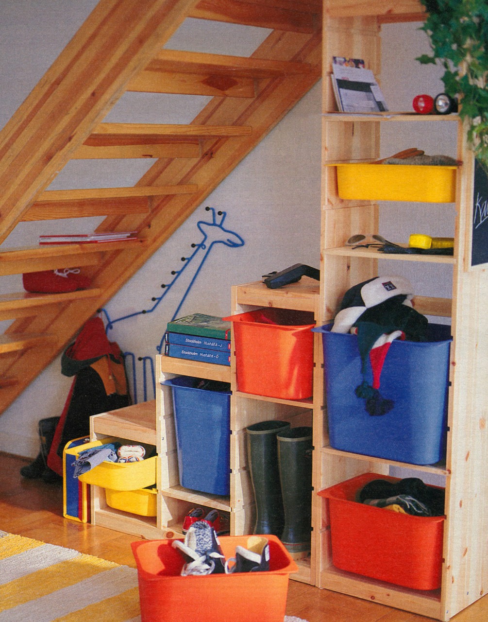 En trappformad förvaringsmöbel i ljust trä och färgglada lådor står i utrymmet under en luftig trappa i ljust trä.
