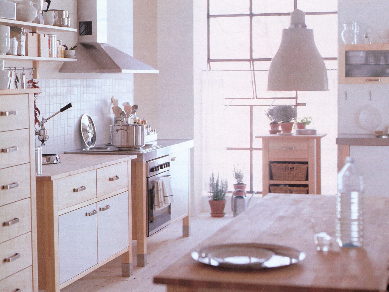 Cuisine en bois clair avec cuisinière, placards et îlot en modules indépendants. Mur carrelé blanc, détails chromés.