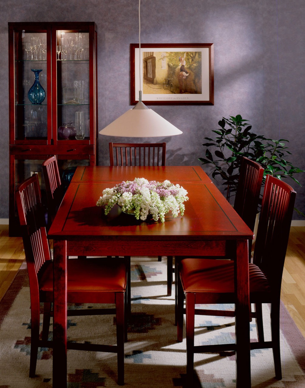 Comedor con larga y mesa de comer y sillas en un tono cerezo, todo en modelo STOCKHOLM, sobre alfombra estampada.