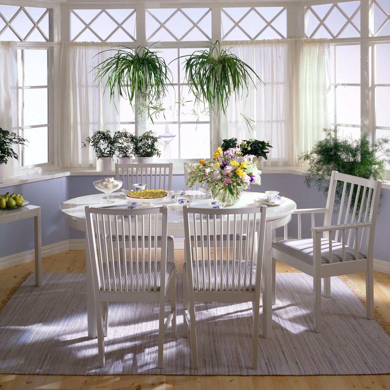 Pinnstolar med och utan armstöd runt ett elliptiskt matbord, allt vitt i modell STOCKHOLM, i ett ljust rum med burspråk.