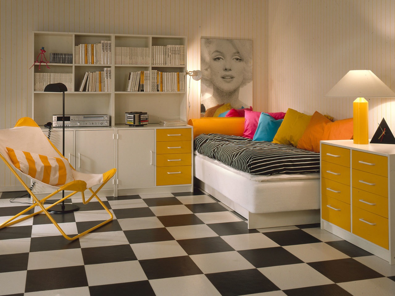 Pièce claire avec sol à damier, tapisserie à rayures jaunes et blanches, meubles de rangement BOJ blancs avec détails jaunes.