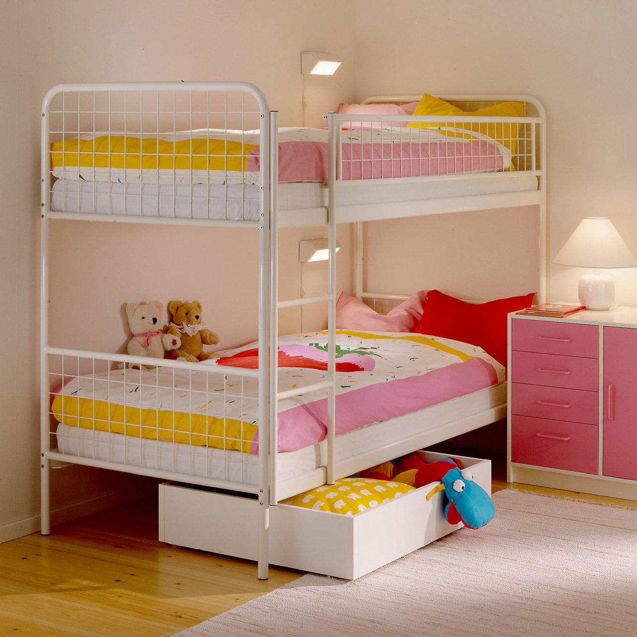 Chambre d’enfant avec lit superposé aux draps bien tirés, autres meubles et détails roses, jaunes et blancs.